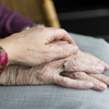 Two hands lie on top of each other. The younger person's hand is on top of the older person. 