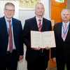 Dr. Franz von Nussbaum, Dr. Andreas Brunschweiger and Prof. Dr. Stefan Laufer stand in a row and smile at the camera. Dr. Brunschweiger holds a certificate in his hand.