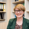 Portrait of a woman with glasses. In the background bookshelves.