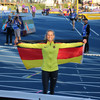 A smiling young woman in sportswear stands in a track and field stadium holding a German flag behind her back.