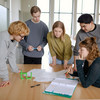 Five students stand around a table and look at a piece of paper.