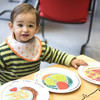 Toddler playing with three children's plates from the dining hall and sitting at a table.