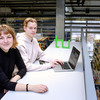 Two students sit at a long table in front of a laptop in the library.