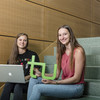 Two students are sitting on a stair. One is holding a laptop and the other the logo of TU Dortmund University