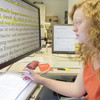 A student sits at a computer reading a text in large print.