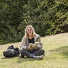 A female student sits cross-legged on a meadow with a book in her hand.