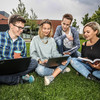 Four students are sitting on the grass and looking in a book.